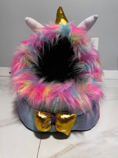 Colorful fuzzy pet bed with unicorn horn and golden bow.